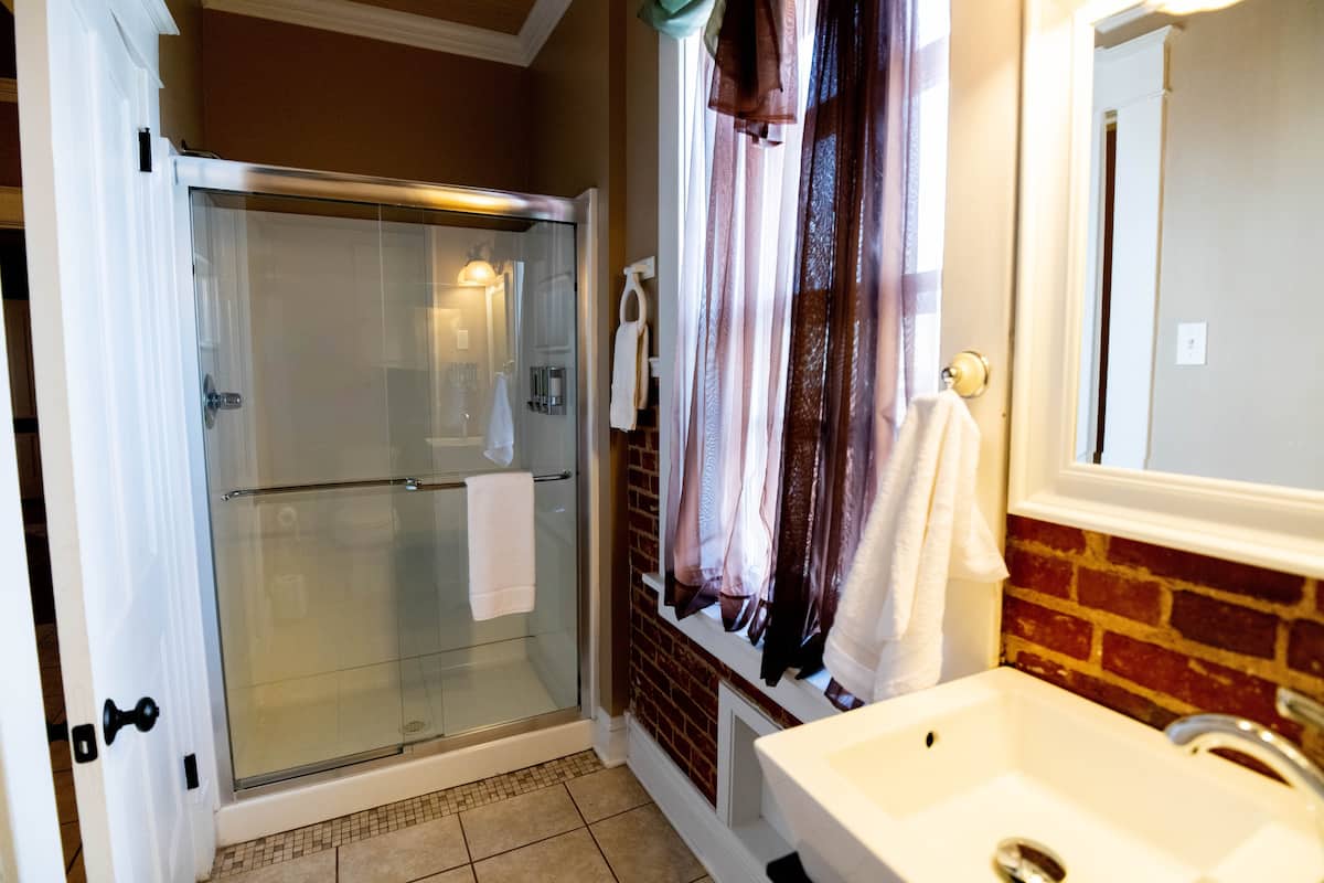 This bathroom features a glass-enclosed shower, a sink with a white basin, a mirror, and exposed brick details, all under warm lighting.