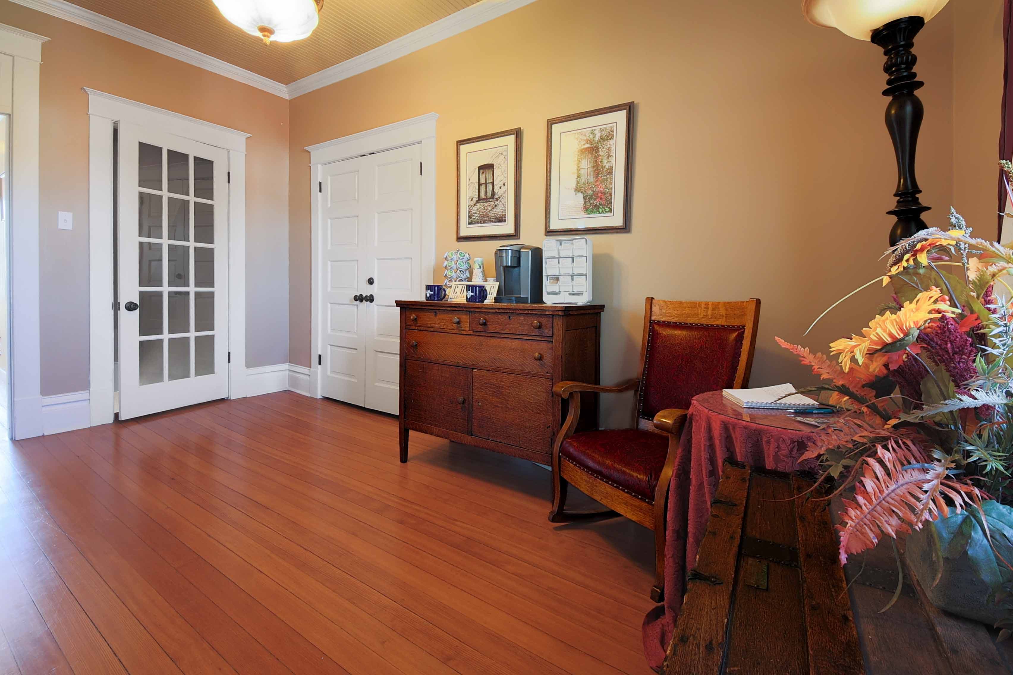 An inviting sitting area featuring gleaming hardwood floors, a dark wood dresser, a wooden chair, and framed art on warm beige walls.