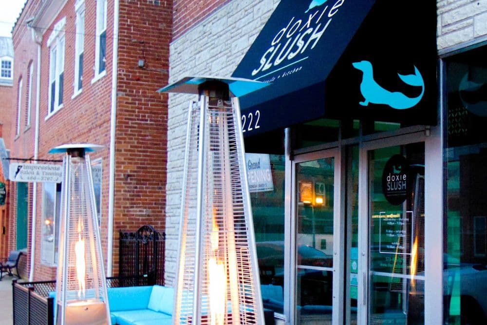 Exterior of Doxie Slush featuring a blue awning, outdoor heaters, and a turquoise seating area.