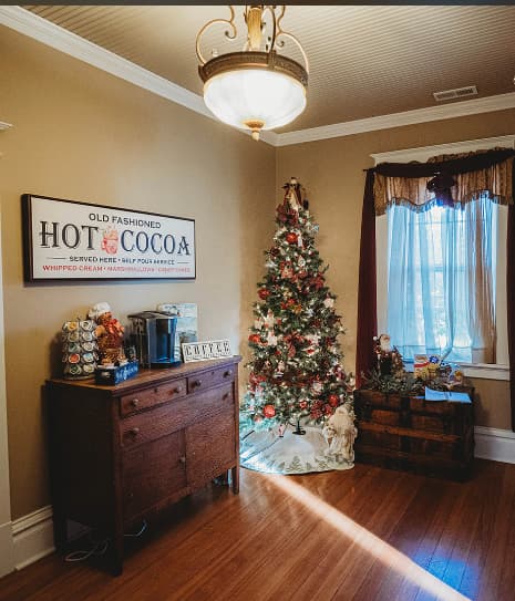 A cozy room featuring a decorated Christmas tree, an old-fashioned hot cocoa sign, and a wooden dresser.
