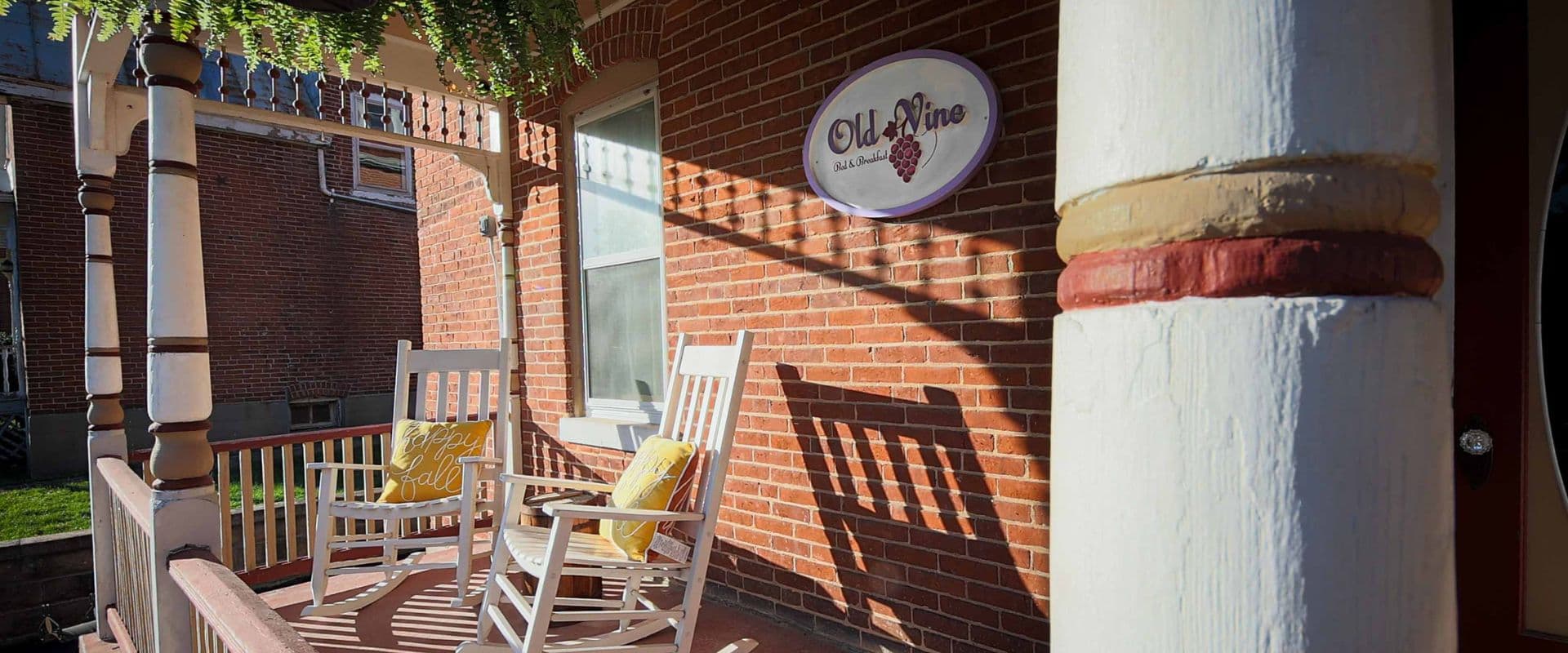 A charming porch with two white rocking chairs and a sign for "Old Nine Bed & Breakfast."