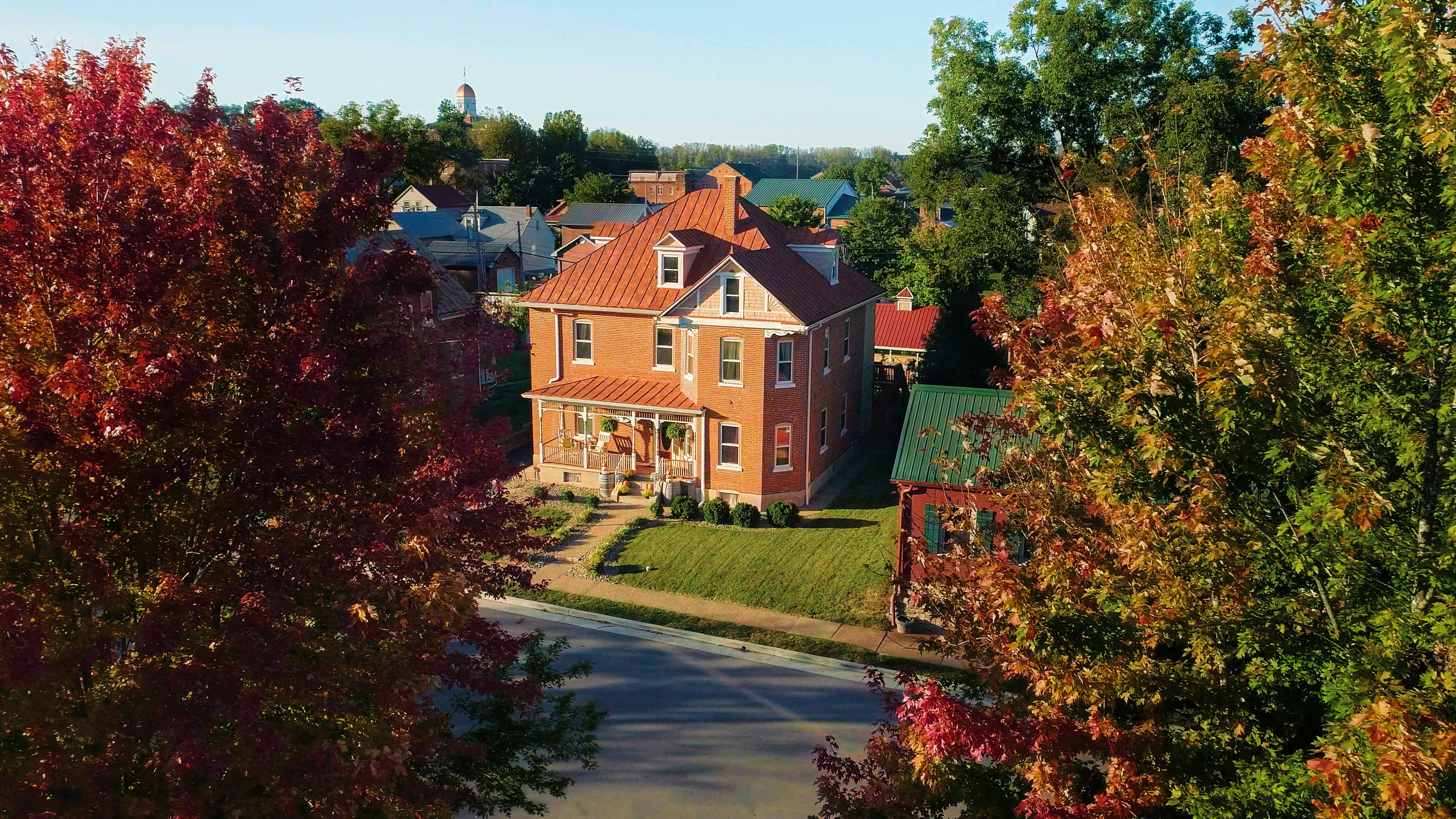 A brick house with a copper roof is surrounded by colorful autumn trees. A brick house with a copper roof is surrounded by colorful autumn trees.