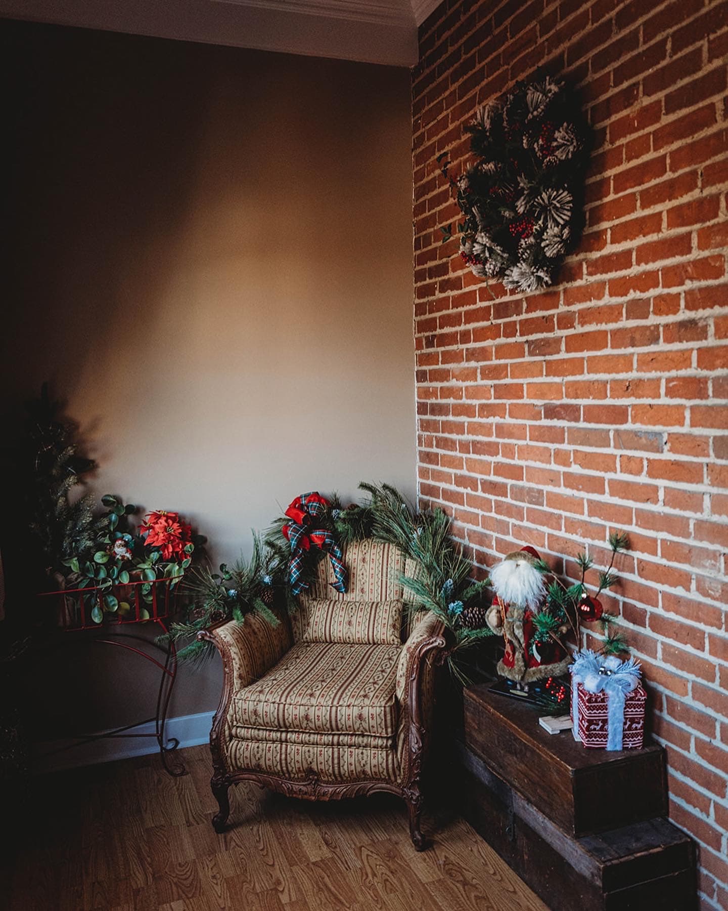 Cozy corner featuring a decorated armchair, holiday wreath, and festive accents against a brick wall.