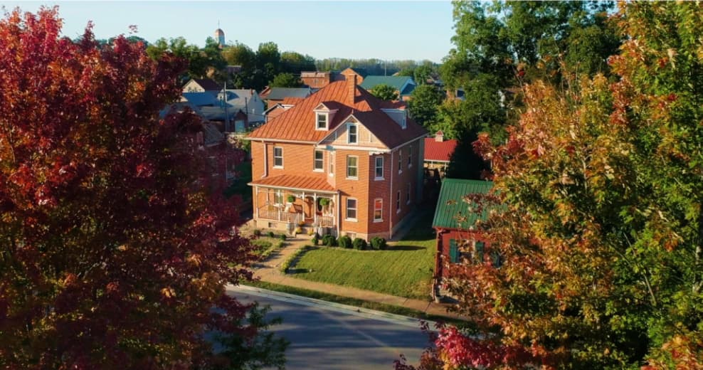 Aerial view of a red-brick house surrounded by colorful autumn trees and greenery. Aerial view of a red-brick house surrounded by colorful autumn trees and greenery.
