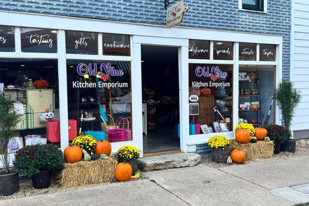 A quaint kitchen store titled "Old Vine Kitchen Emporium" displays pumpkins and flowers outside its welcoming entrance.