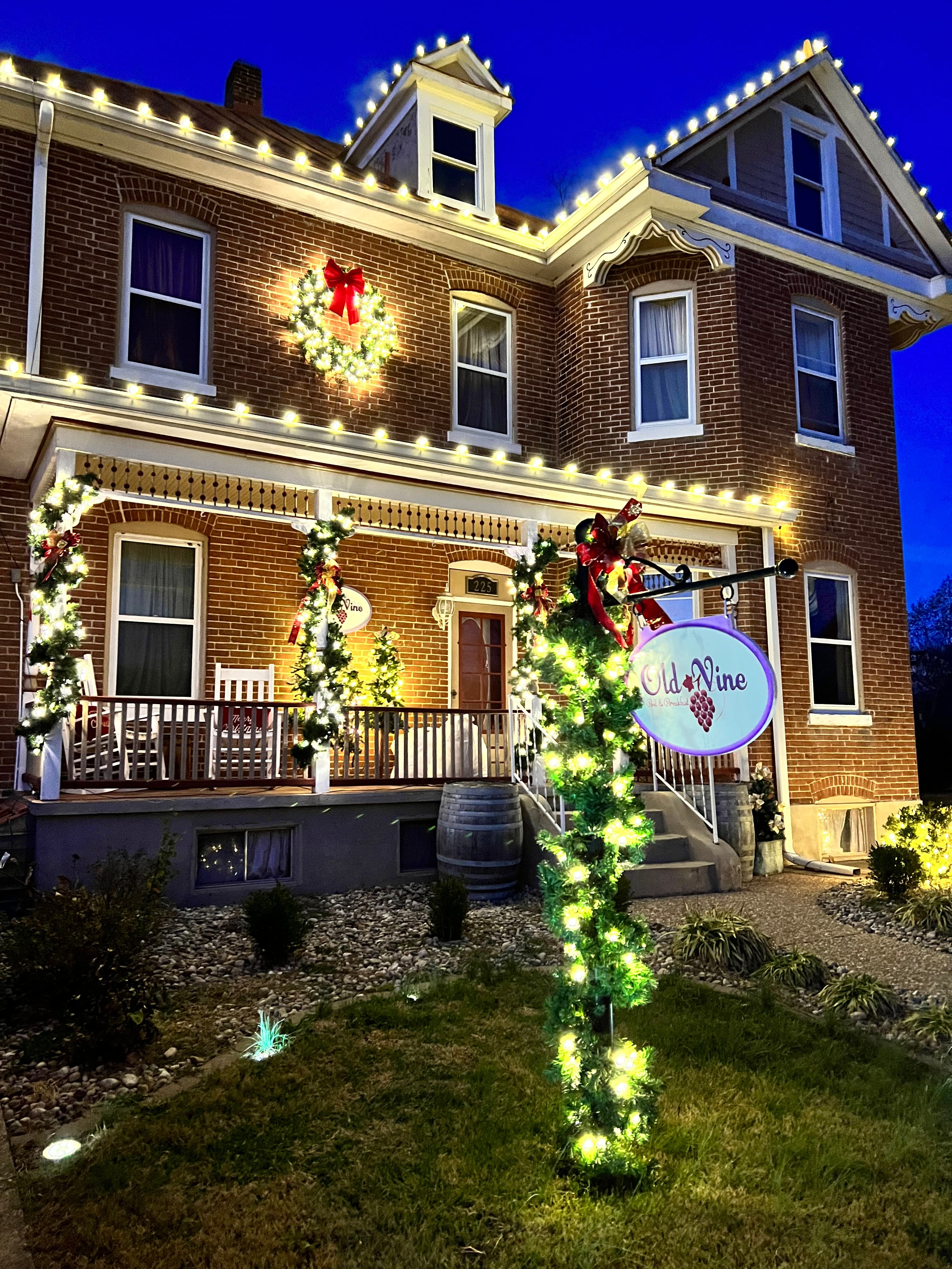 A beautifully decorated brick house adorned with holiday lights and a festive wreath at dusk.