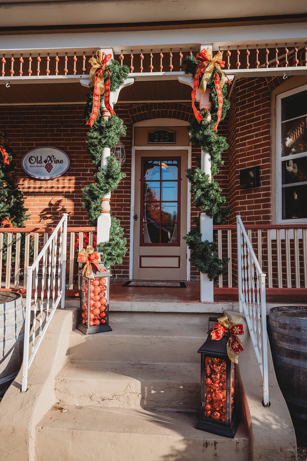 Festively decorated porch with garlands and lanterns at a brick-fronted building.